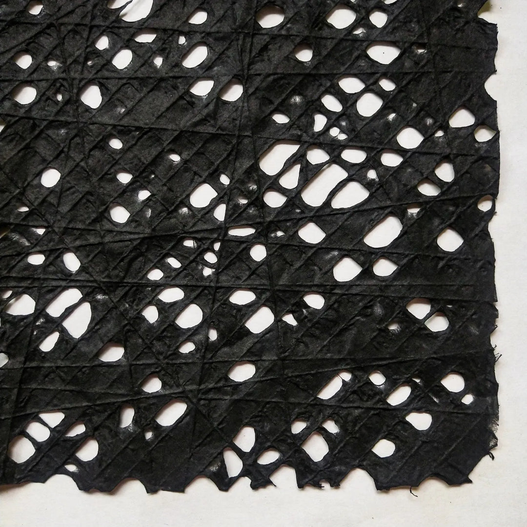 Detailed view of black handmade paper crafted at Kozo Studio, featuring a fishnet pattern formed by individually placed cotton threads on mulberry pulp.