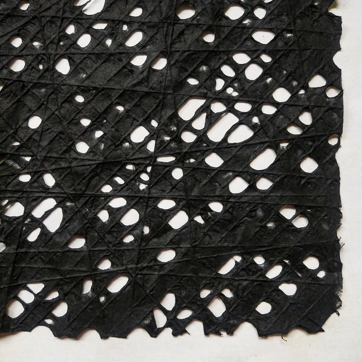 Detailed view of black handmade paper crafted at Kozo Studio, featuring a fishnet pattern formed by individually placed cotton threads on mulberry pulp.