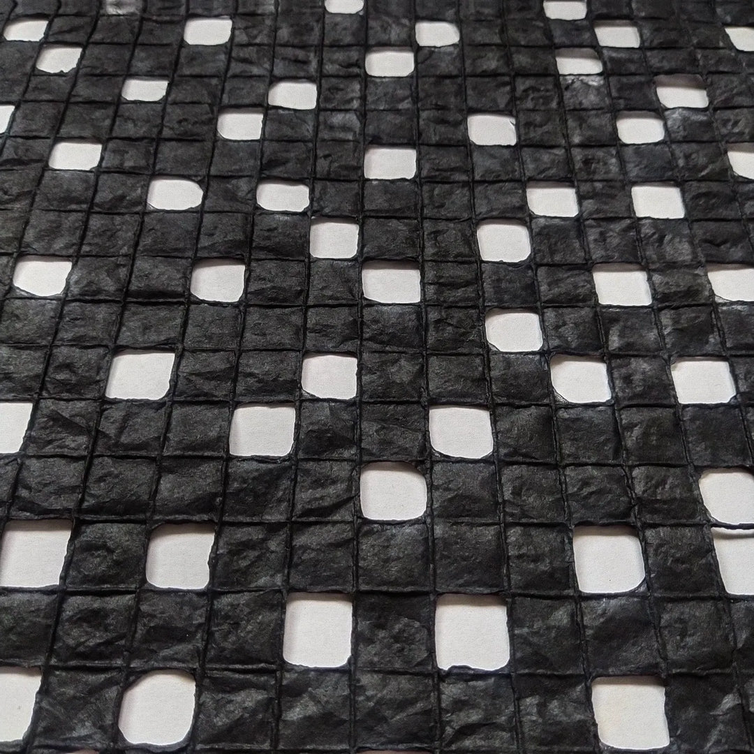 Close-up of black handmade mulberry paper crafted at Kozo Studio, showcasing a checkered design formed with fine cotton lines.