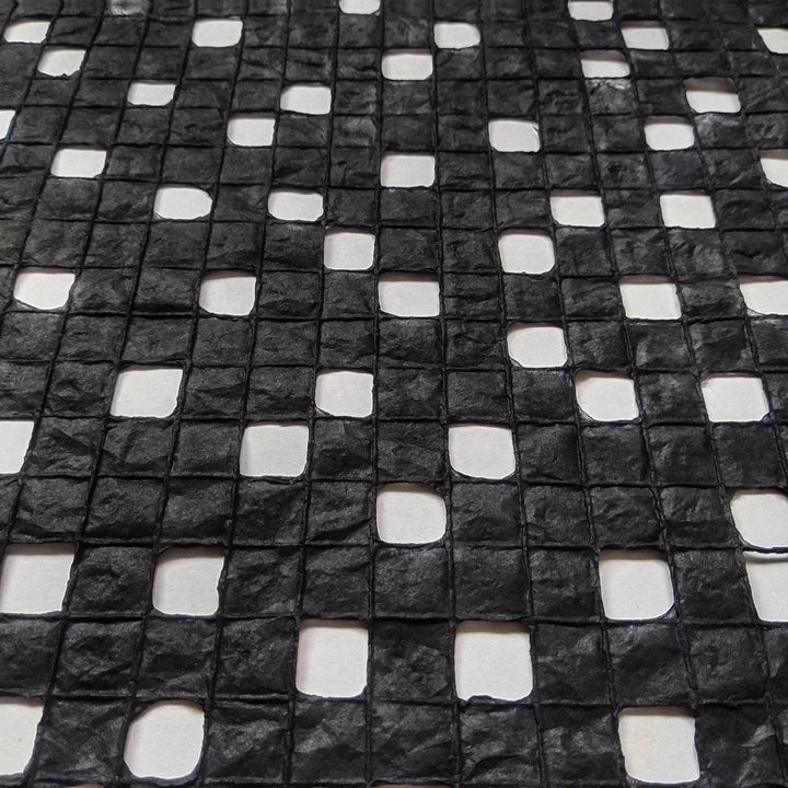 Close-up of black handmade mulberry paper crafted at Kozo Studio, showcasing a checkered design formed with fine cotton lines.