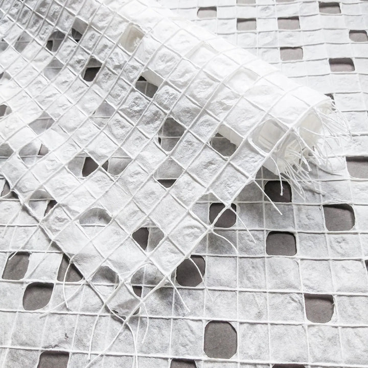 White handmade paper crafted from mulberry pulp at Kozo Studio, featuring a delicate checkered pattern formed by hand-drawn cotton threads.