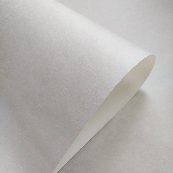 Close-up of Kozo Studio handmade paper sheet, white mulberry paper 70 gsm, with smooth texture and curled edge, ideal for art and printmaking.