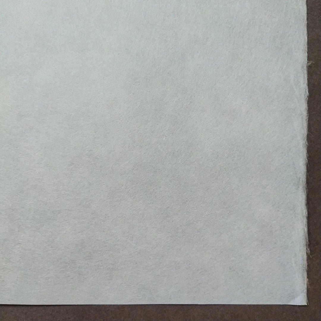 A close-up shows a sheet of White Kozo Paper (70 gsm, 64x94 cm) from Kozo Studio with a slightly textured surface against a dark brown background; the papers edge is visible on the right.