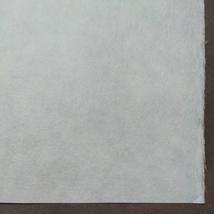 A close-up shows a sheet of White Kozo Paper (70 gsm, 64x94 cm) from Kozo Studio with a slightly textured surface against a dark brown background; the papers edge is visible on the right.