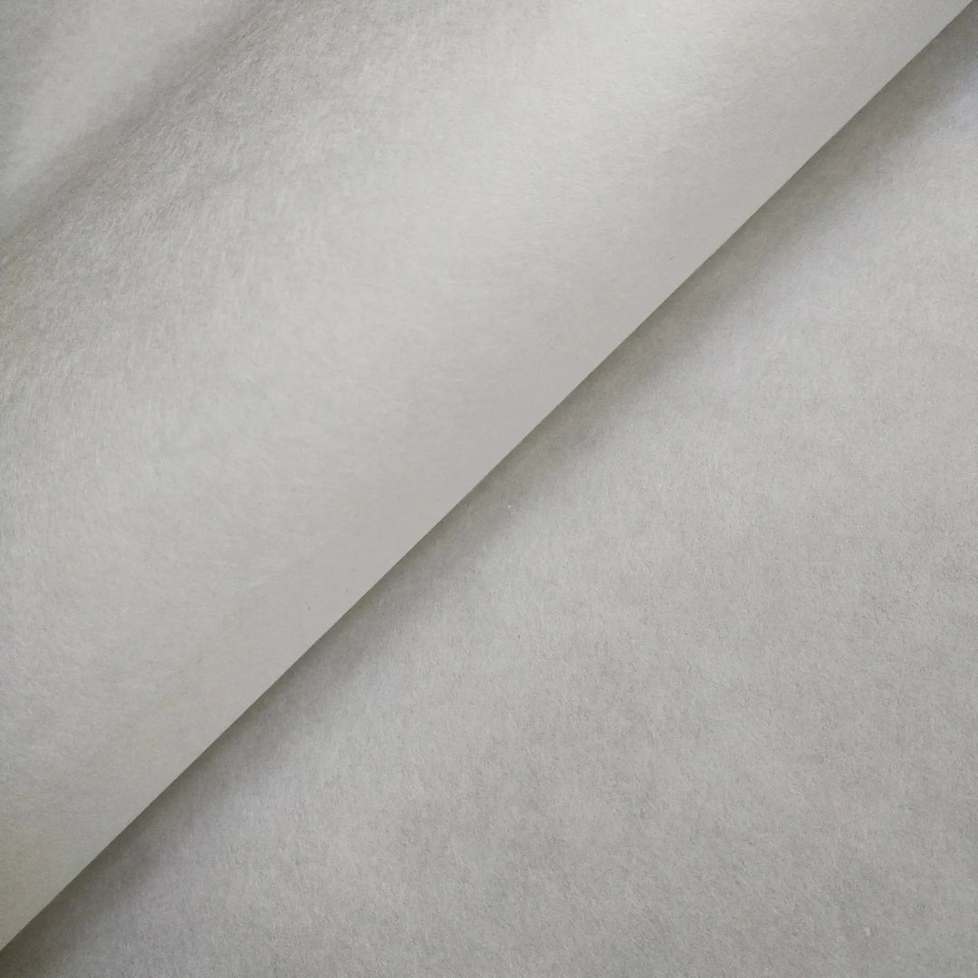 An angled close-up of a single sheet of White Kozo Paper (70 gsm, 64x94 cm) by Kozo Studio shows its smooth, subtly reflective surface with shadows highlighting the unique texture.