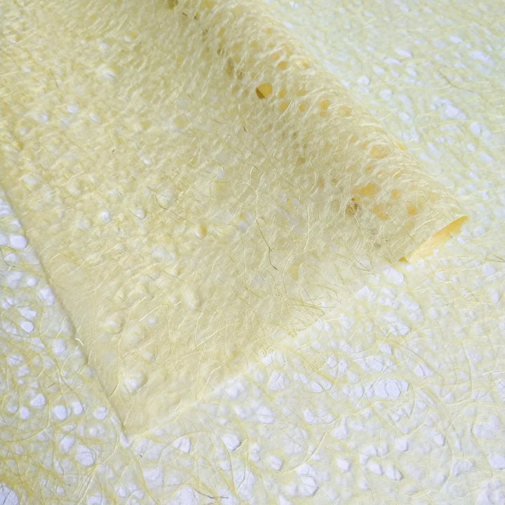Artistic image of yellow Asarakusui Lace Paper from Kozo Studio, a fine handmade mulberry paper known for its visible fiber patterns and lightweight texture.