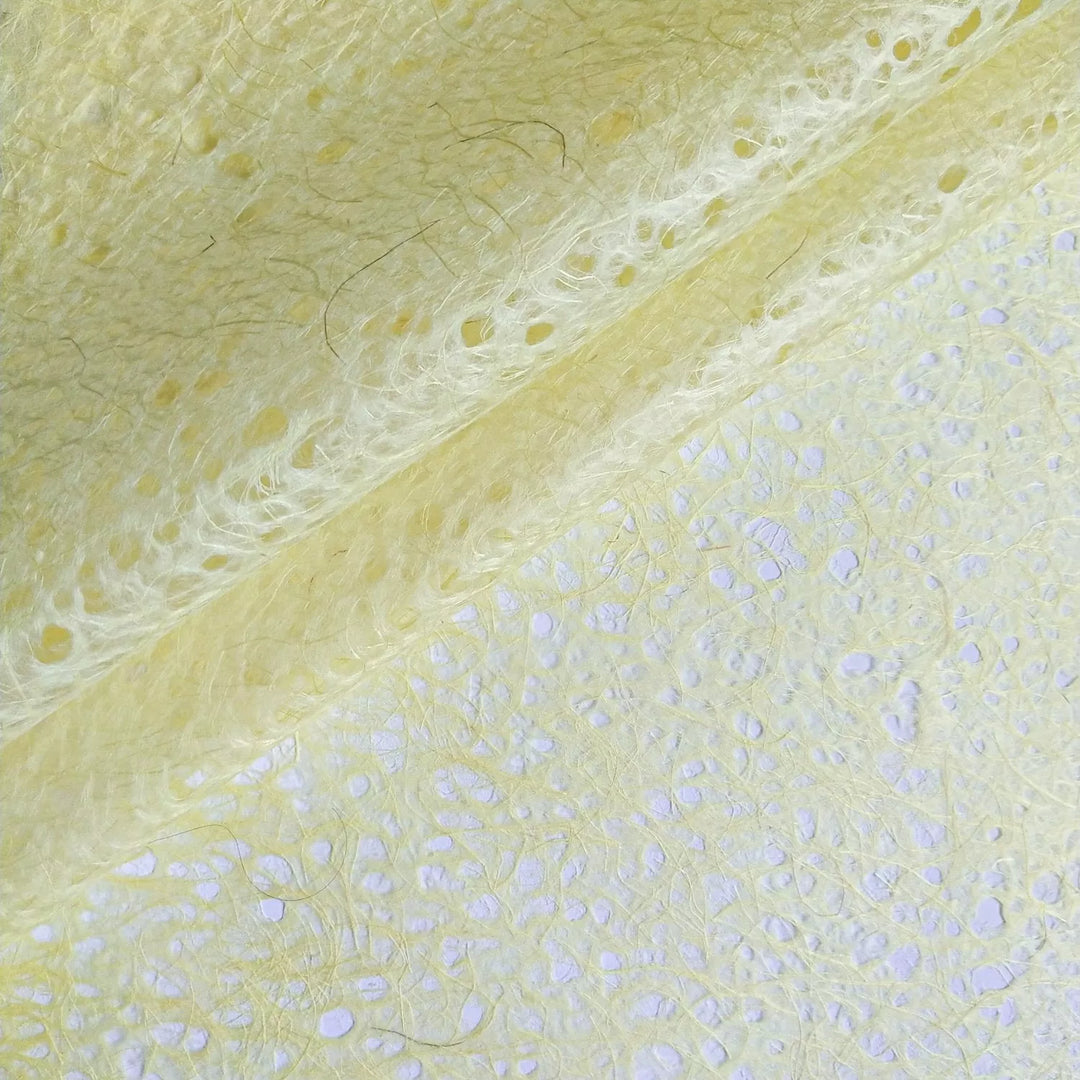Macro shot of handmade mulberry paper by Kozo Studio, rolled to display its soft translucency and fibrous surface with delicate organic lace details.