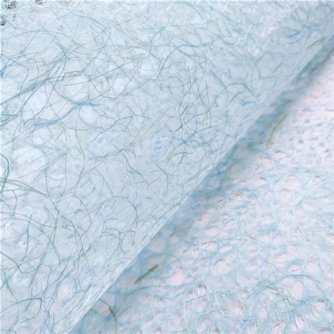 Close-up of light blue handmade paper by Kozo Studio, featuring translucent mulberry paper texture with delicate, swirling web-like fibers.