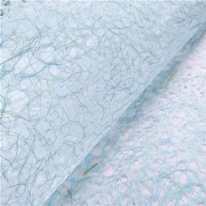 Close-up of light blue handmade paper by Kozo Studio, featuring translucent mulberry paper texture with delicate, swirling web-like fibers.