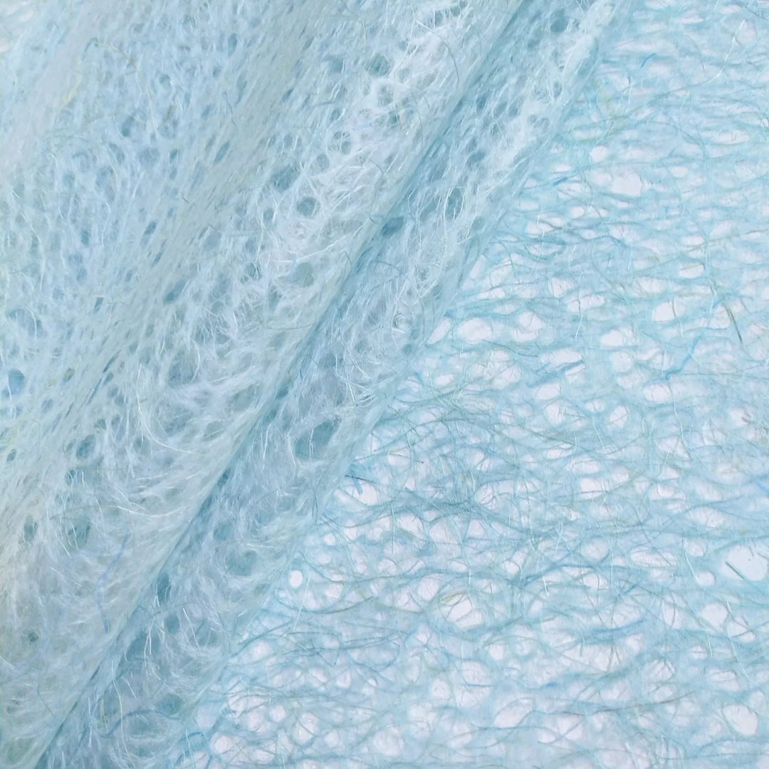 Translucent handmade mulberry paper from Kozo Studio in light blue, with swirling lace-like fibers and a delicate organic appearance.