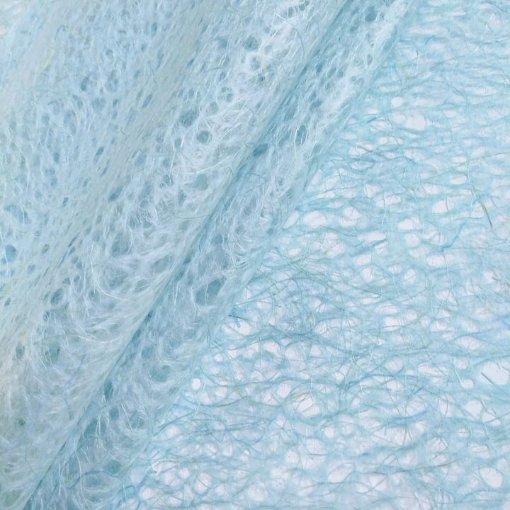 Translucent handmade mulberry paper from Kozo Studio in light blue, with swirling lace-like fibers and a delicate organic appearance.