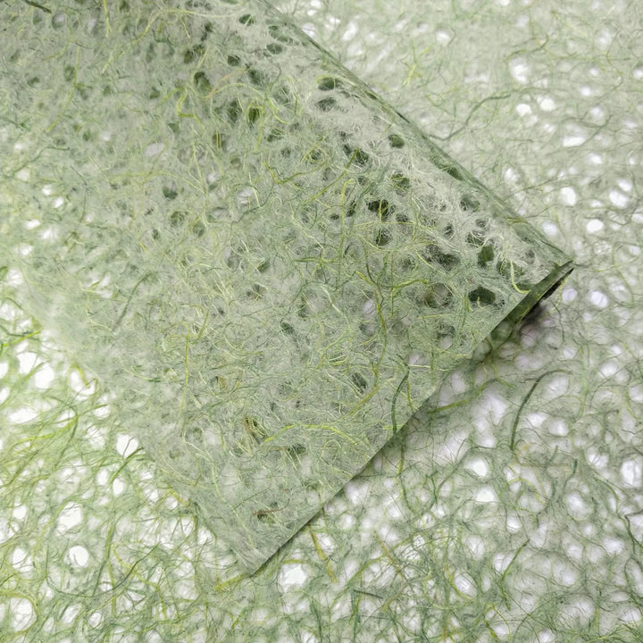 Zoomed view of green handmade mulberry paper from Kozo Studio with visible fibrous structure and lace-like Asarakusui design.