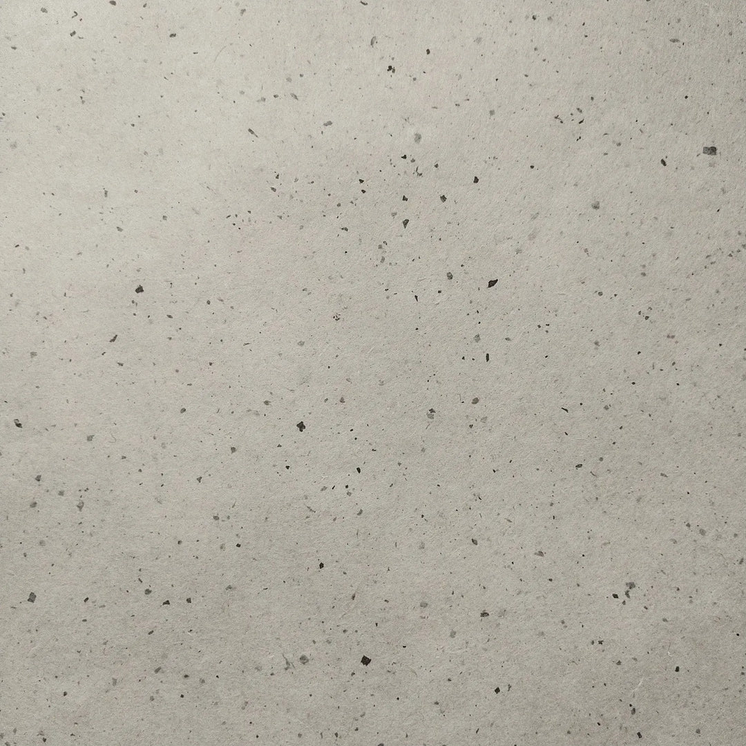 Handmade mulberry paper from Kozo Studio, folded gently over a light background, showcasing the natural texture and speckled surface of Chiri Kozo Paper Natural.