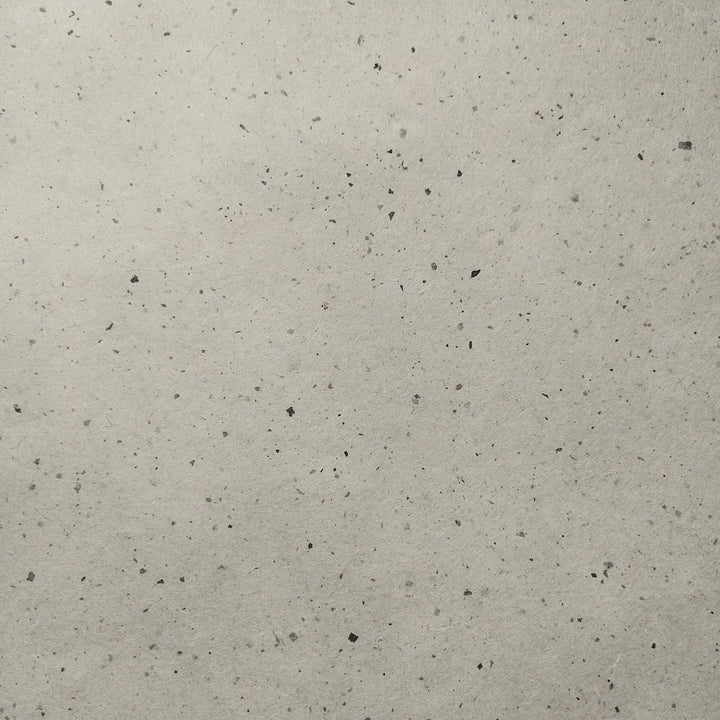 Handmade mulberry paper from Kozo Studio, folded gently over a light background, showcasing the natural texture and speckled surface of Chiri Kozo Paper Natural.