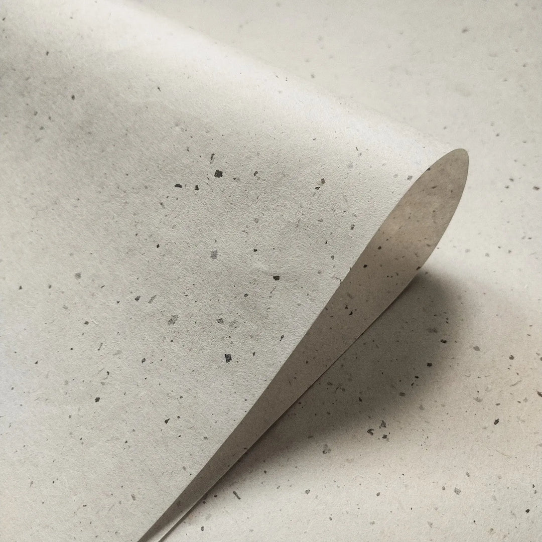 A partially folded sheet of Chiri Kozo Paper Natural by Kozo Studio displays its delicate handmade paper texture and off-white mulberry paper tone with scattered grey flecks.