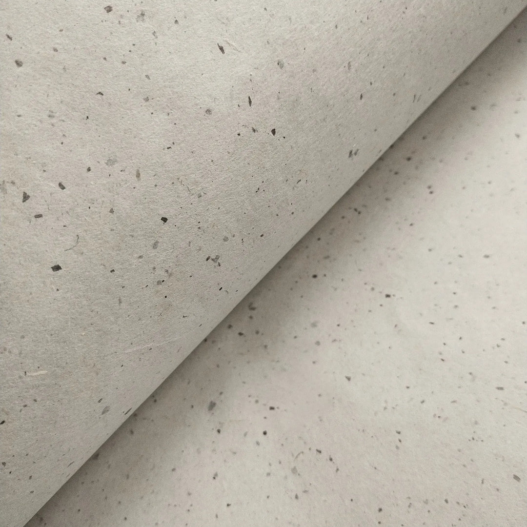A close-up of off-white Chiri Kozo handmade paper from Kozo Studio, folded to reveal the unique speckled texture of traditional mulberry paper.