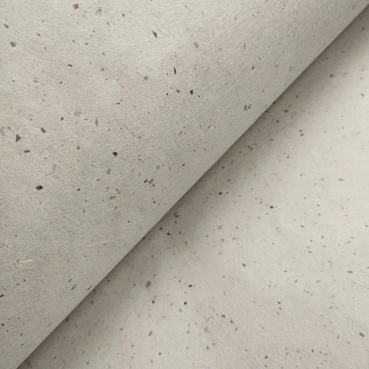 A close-up of off-white Chiri Kozo handmade paper from Kozo Studio, folded to reveal the unique speckled texture of traditional mulberry paper.
