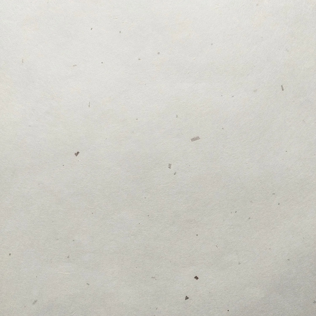 A close-up of the Chiri Kozo Paper White (45 gsm) by Kozo Studio, showcasing its plain, textured surface with small specks and visible fibers of mulberry paper.