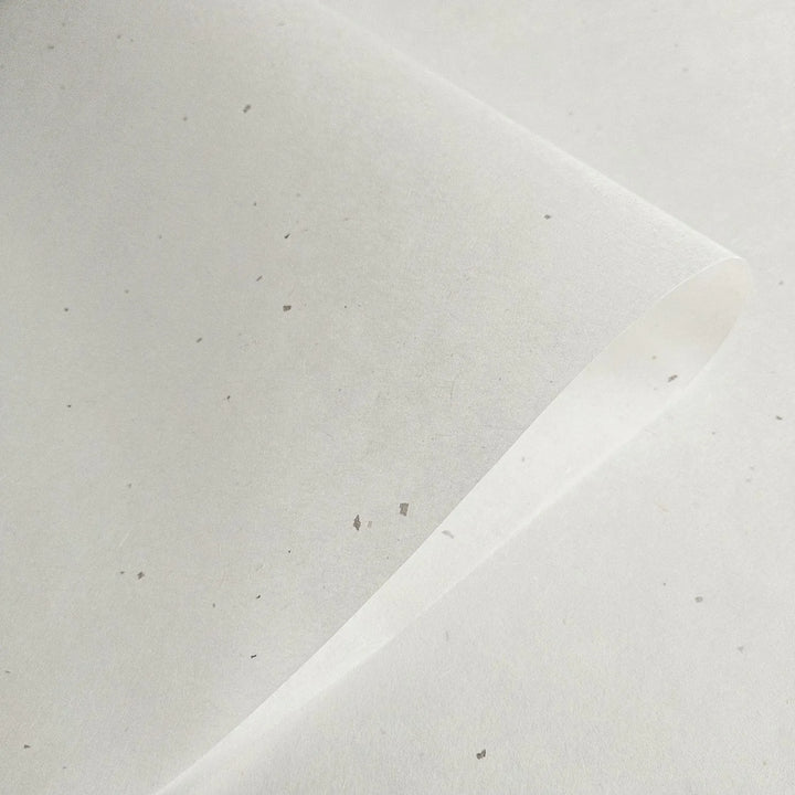 A close-up of Chiri Kozo Paper White (45 gsm) by Kozo Studio highlights its textured mulberry surface with small specks. A slightly curled top corner adds depth to the image.