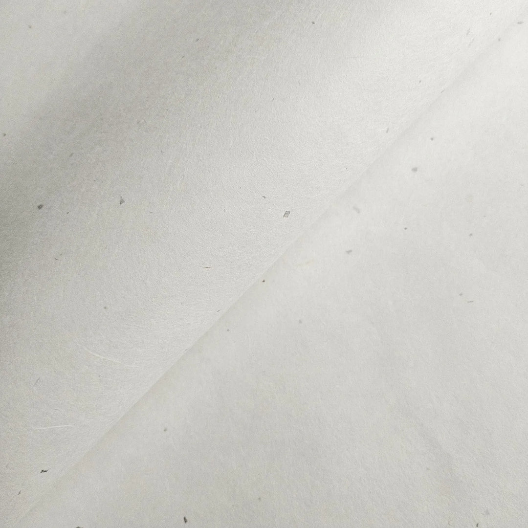 A close-up of Chiri Kozo Paper White by Kozo Studio reveals its off-white, fibrous mulberry texture with a diagonal crease and slight speckles, highlighting its natural, handcrafted quality.