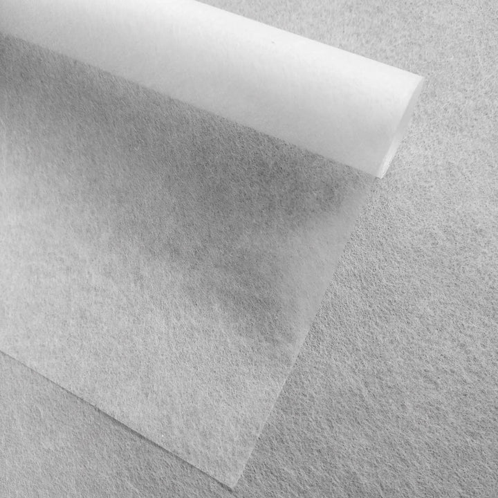 A close-up photo of Kozo Studio Conservator No.1 washi paper (8.5 gsm, 15 sheets/pack) partially rolled on a textured light gray surface, highlighting the contrast between its smooth translucence and the rough background.