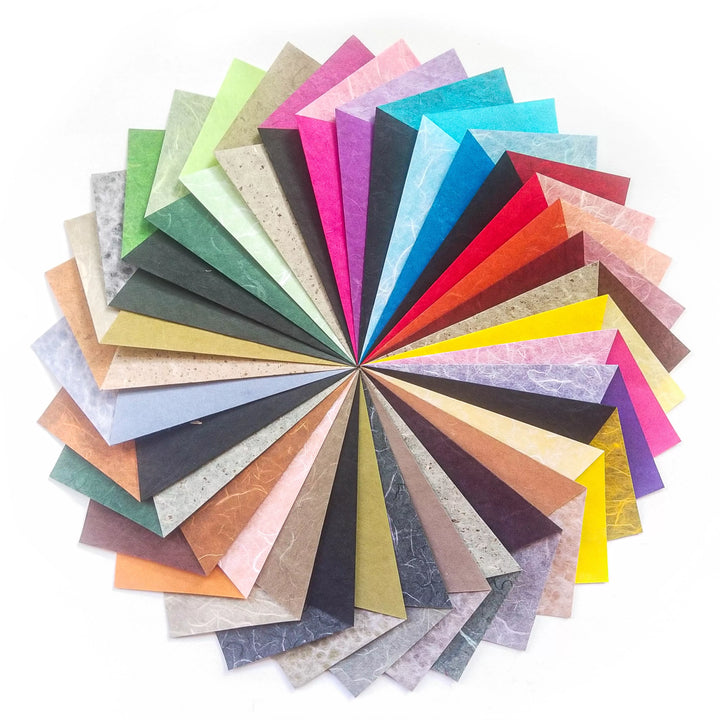The Origami Duo Kozo Paper Pack by Kozo Studio features a circular display of 6x6 inch multicolored sheets, fanned out like a rainbow in hues of pink, blue, green, yellow, and brown against a white background.