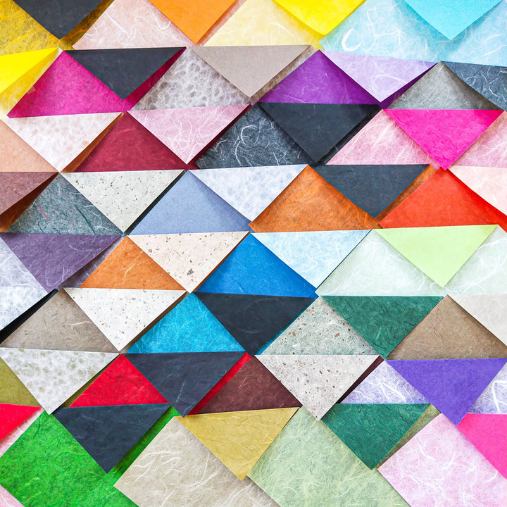 The Origami Duo Kozo Paper Pack from Kozo Studio features vibrant geometric patterns of overlapping squares and triangles in blue, red, yellow, green, and purple. Crafted from textured mulberry paper, it creates a stunning three-dimensional mosaic effect.