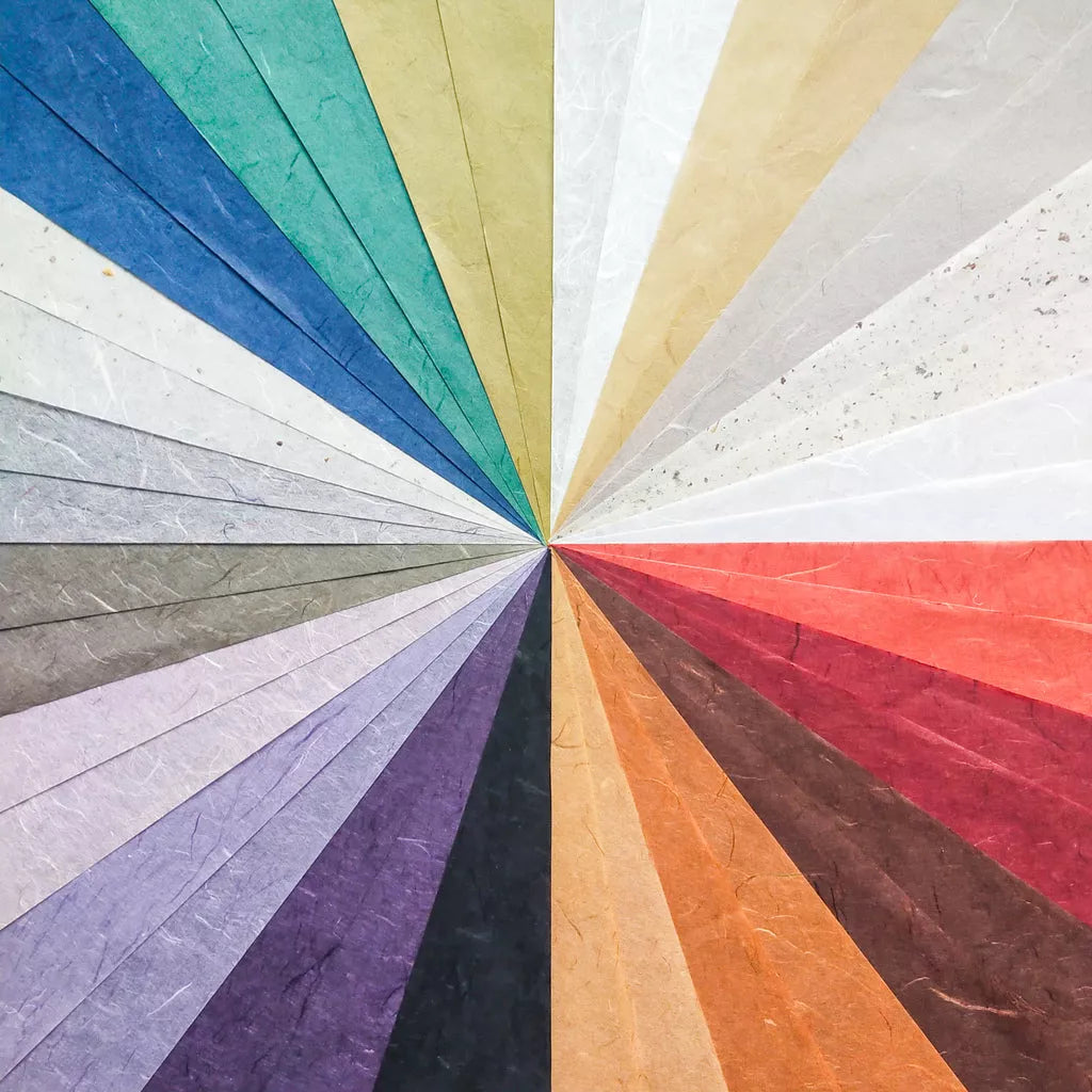The Assorted A4 Earth Unryu Kozo Paper Set from Kozo Studio features a top-down view of a colorful, radial pattern using various mulberry paper textures. The papers fan out, showcasing blues, greens, reds, and neutrals for a vibrant and visually appealing design.