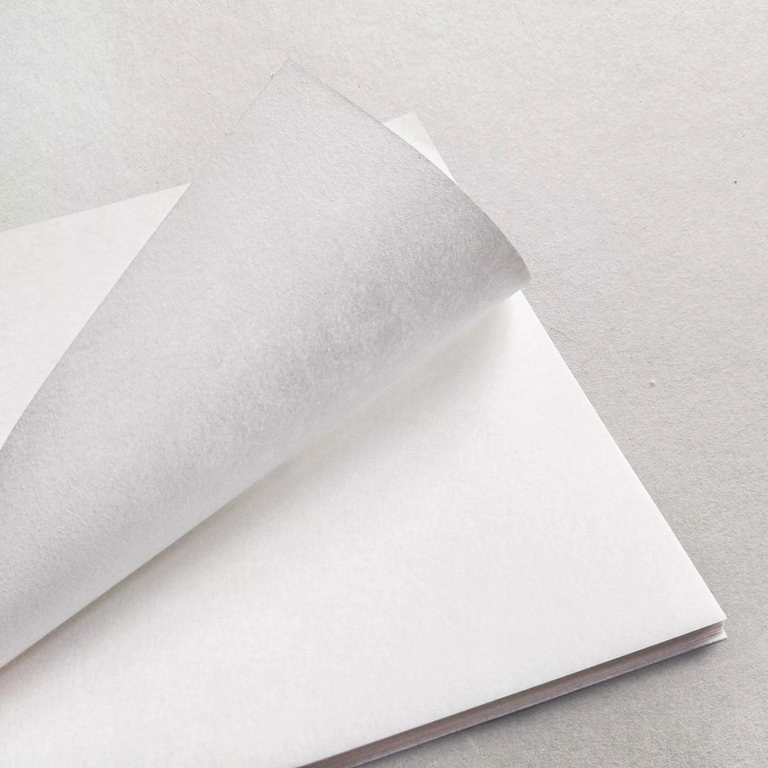 A close-up of Kozo Studios A4 Decoupage Plain Mulberry Paper (40 Sheets, 30 gsm) shows a stack of eco-friendly white sheets with the top sheet partially lifted, displayed on a light-colored surface.