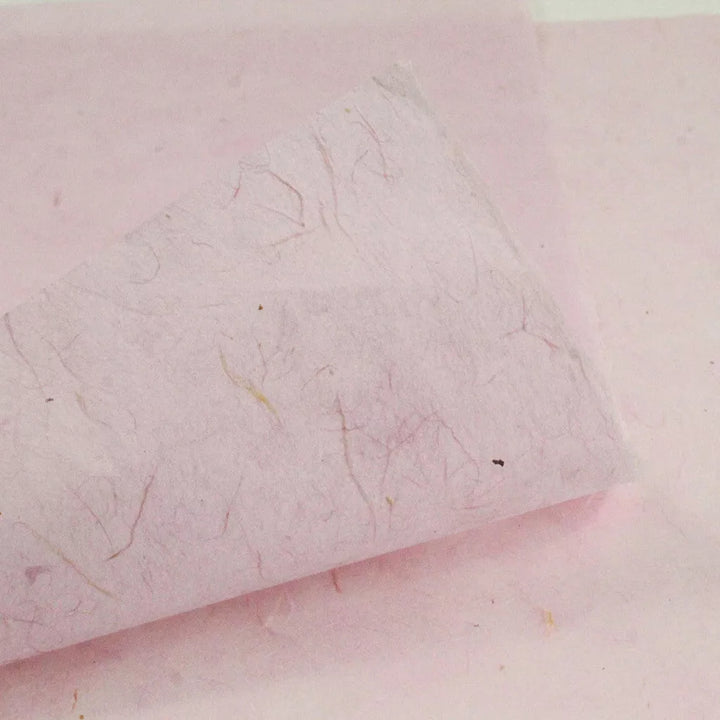 Close-up of Kozo Studios Water-resistant Kozo Paper in pink, featuring visible fibers and a slightly curled corner. The soft surface has subtle color variations, of traditional rice paper textures.
