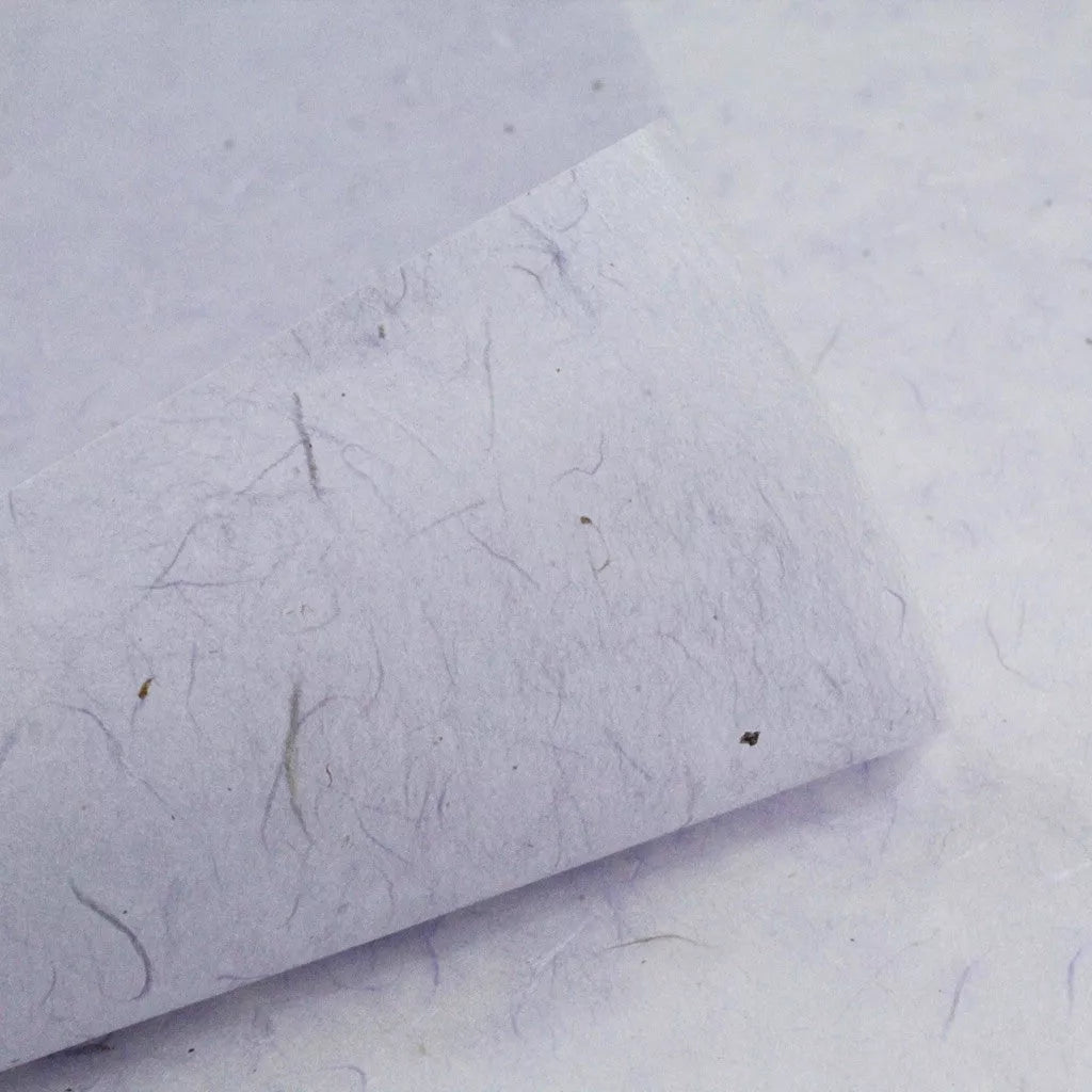 Close-up of Kozo Studios Water-resistant Kozo Paper in Lavender, showcasing its textured finish with visible fibers and specks. The off-white surface appears slightly rough, with a corner turned up to reveal the layer beneath.
