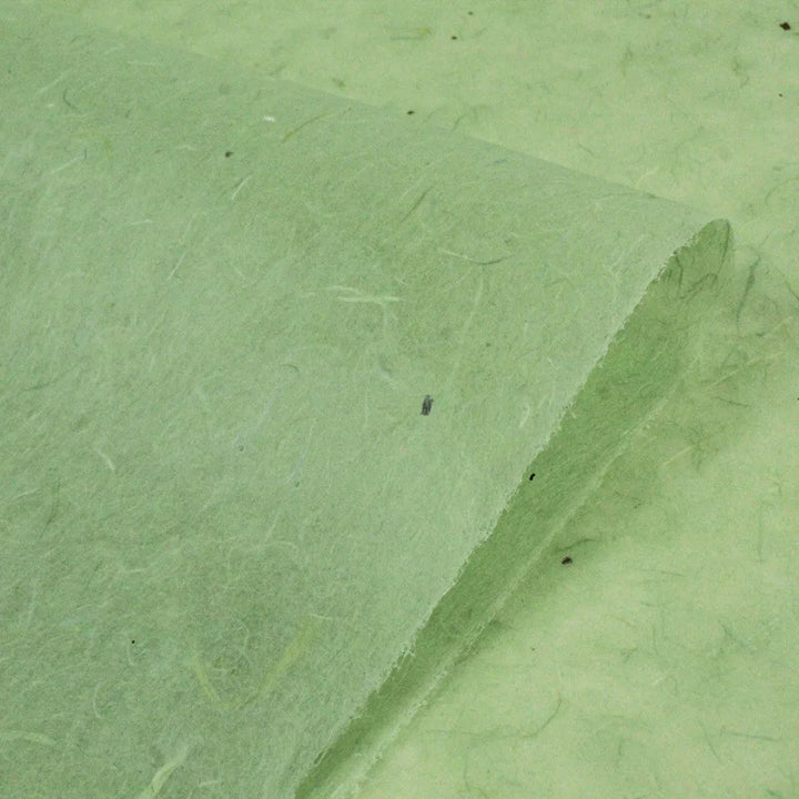Close-up of a sheet of Kozo Studios water-resistant mint Kozo Paper, showcasing its handmade rough texture with visible fibers and specks for a natural look. The sheet is partially folded over itself.