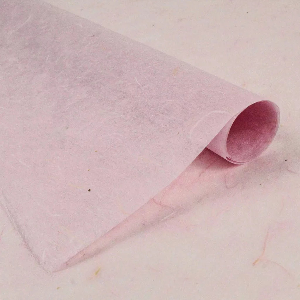 A close-up of a partially rolled sheet of Kozo Studios water-resistant pink Kozo Paper reveals a soft, fibrous texture of rice paper, with visible plant fibers woven throughout.