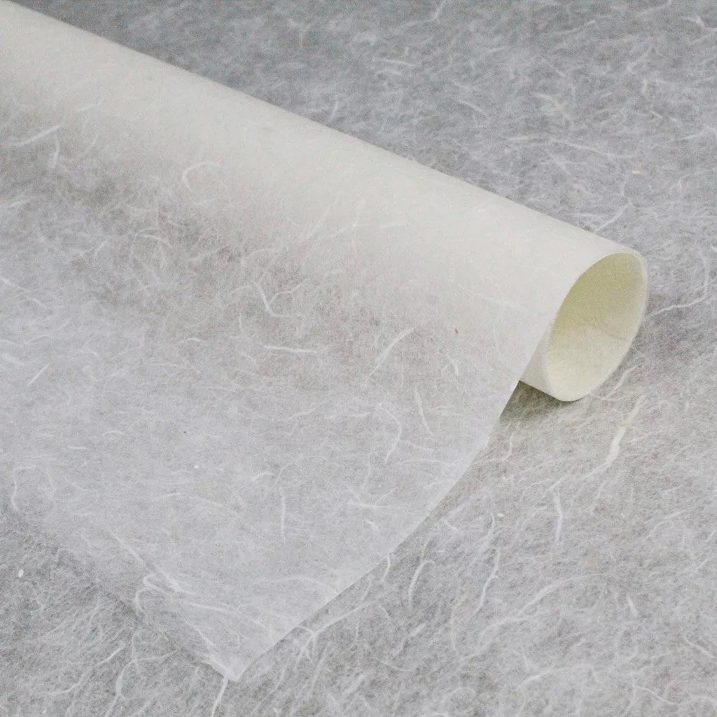 A close-up of a partially unrolled roll of Kozo Studios Water-resistant Kozo Paper (White) on a matching surface highlights its textured, fibrous appearance, creating a subtle, speckled pattern akin to fine rice paper craftsmanship.