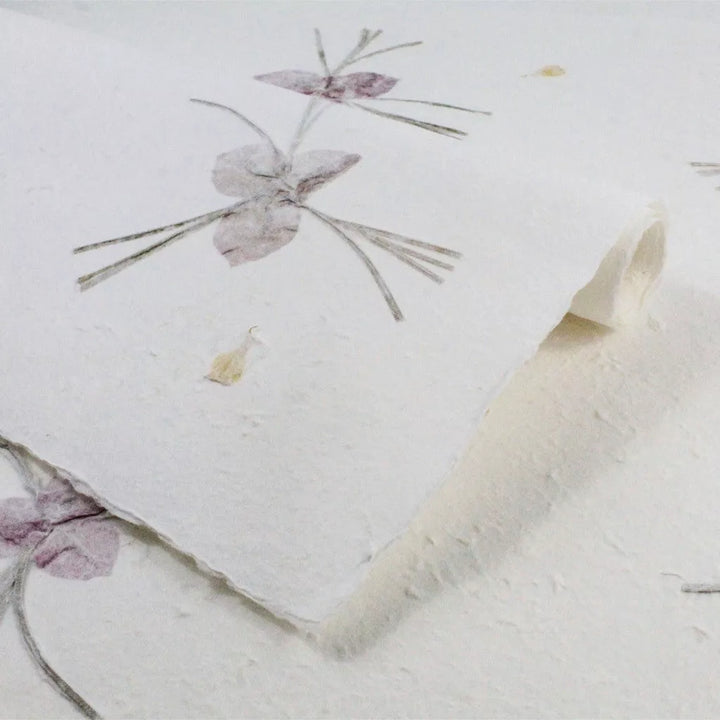 Handmade paper with delicate purple flowers and curled edges, crafted by Kozo Studio using traditional mulberry paper techniques.