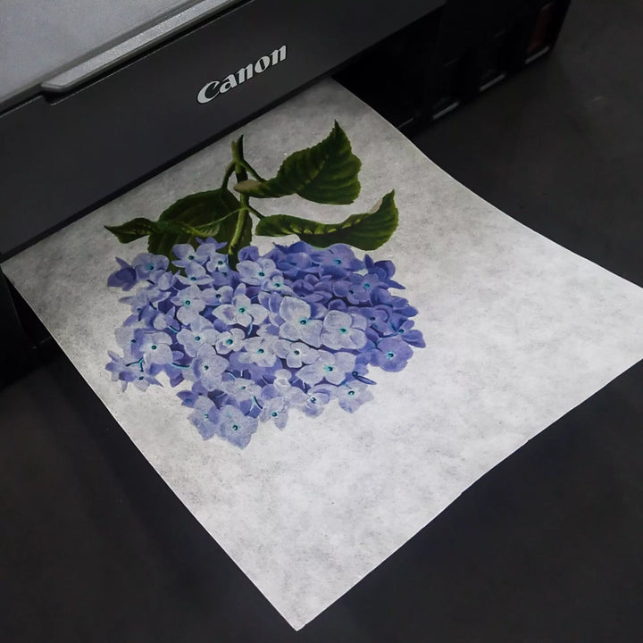 A Canon printer expertly prints a hydrangea bouquet with green leaves on A4 Extra Thin White Kozo Paper from Kozo Studio. The flowers, in light purple and blue shades, beautifully stand out against the dark background.