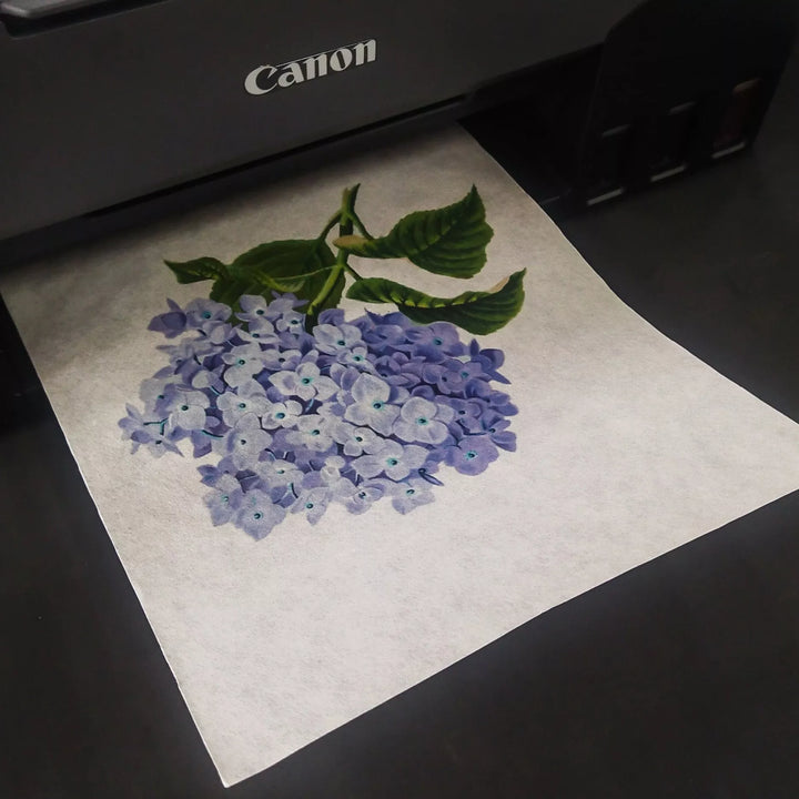 A printer is delivering an image of a floral bouquet with blue and purple hydrangeas on Kozo Studios A4 Extra Thin Natural Kozo Paper, featuring green leaves and delicately crafted detail.