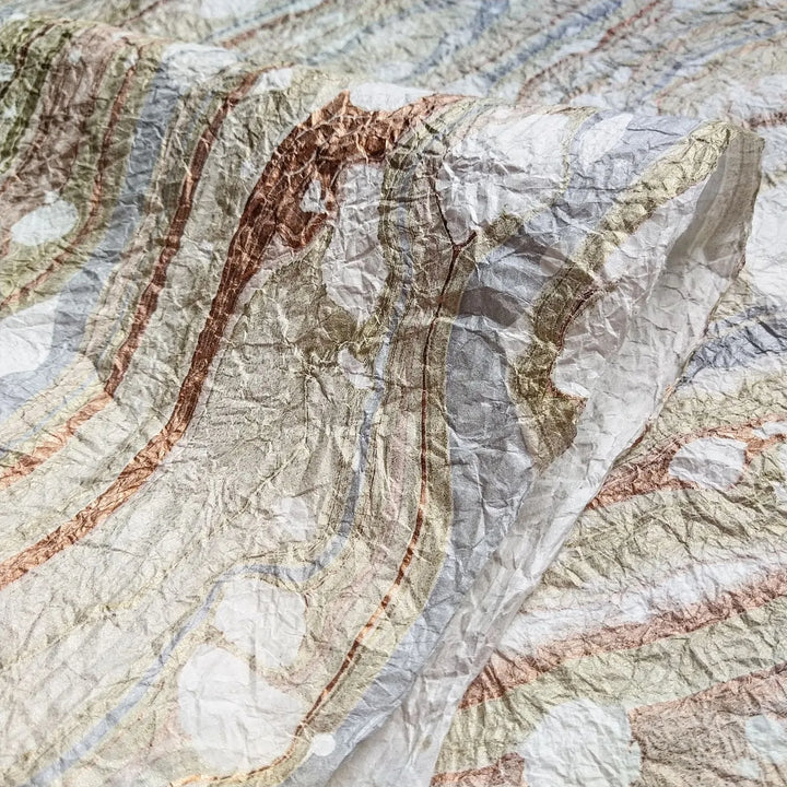 A close-up of Milano Kozo Paper - Design 10 (White) by Kozo Studio reveals swirling, marbled patterns and Mulberry textures in earthy tones reminiscent of a topographic map, with layered flowing lines adding depth and a tactile quality.