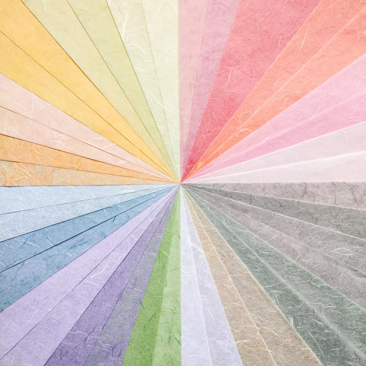 The Assorted A4 Pastel Unryu Kozo Paper Set by Kozo Studio features a radial display of textured mulberry sheets fanning out in warm yellows, pinks, and cool blues and grays, converging at a central point to create a vibrant gradient.