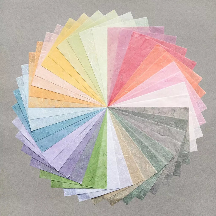 The Assorted A4 Pastel Unryu Kozo Paper Set by Kozo Studio, featuring textured mulberry sheets in yellow, pink, orange, blue, green, and gray hues, is arranged spirally against a plain gray background.