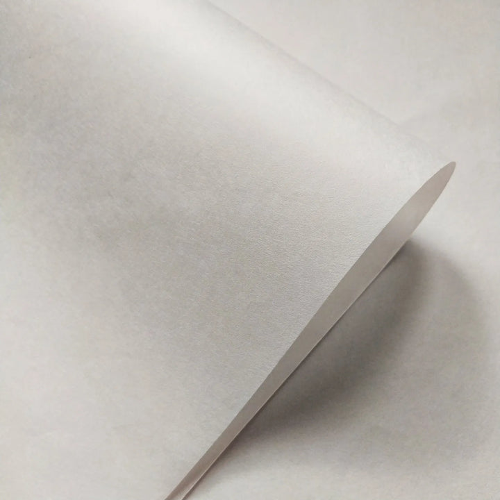 A close-up of a Thin White Kozo Paper Roll (45 gsm) by Kozo Studio, slightly curled at the edge on a smooth white surface, with lighting emphasizing the kozo fiber texture and gentle curve.