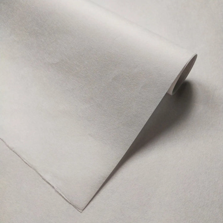 A close-up of a Thin White Kozo Paper Roll (45 gsm) by Kozo Studio shows its slight texture and delicate rolled corner—perfect for printmaking enthusiasts.