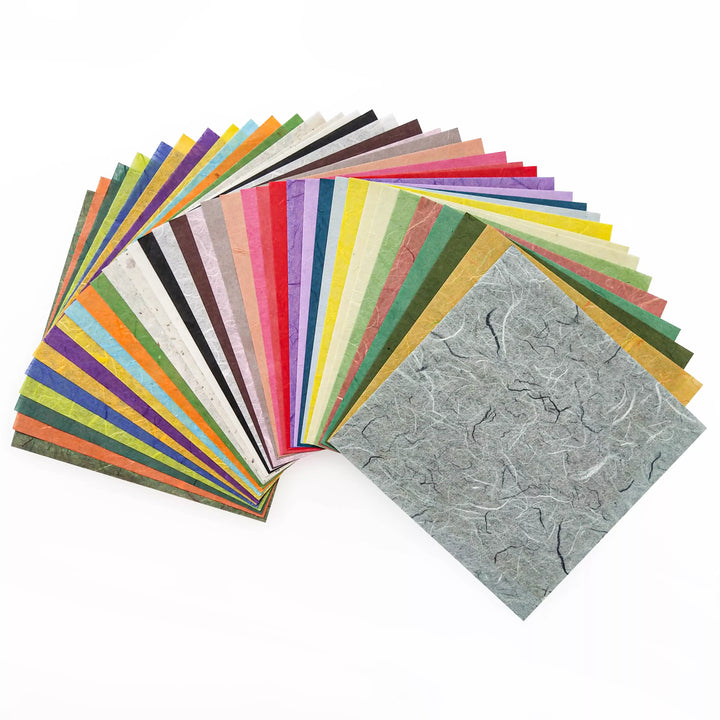 The Origami Unryu Kozo Paper Pack (6x6 in., 72 sheets) from Kozo Studio fans out in a semicircle, offering colorful and textured sheets. The exotic charm of Mulberry and Rice Papers adds variety with vibrant to subdued tones, while the front sheets crumpled texture stands out.