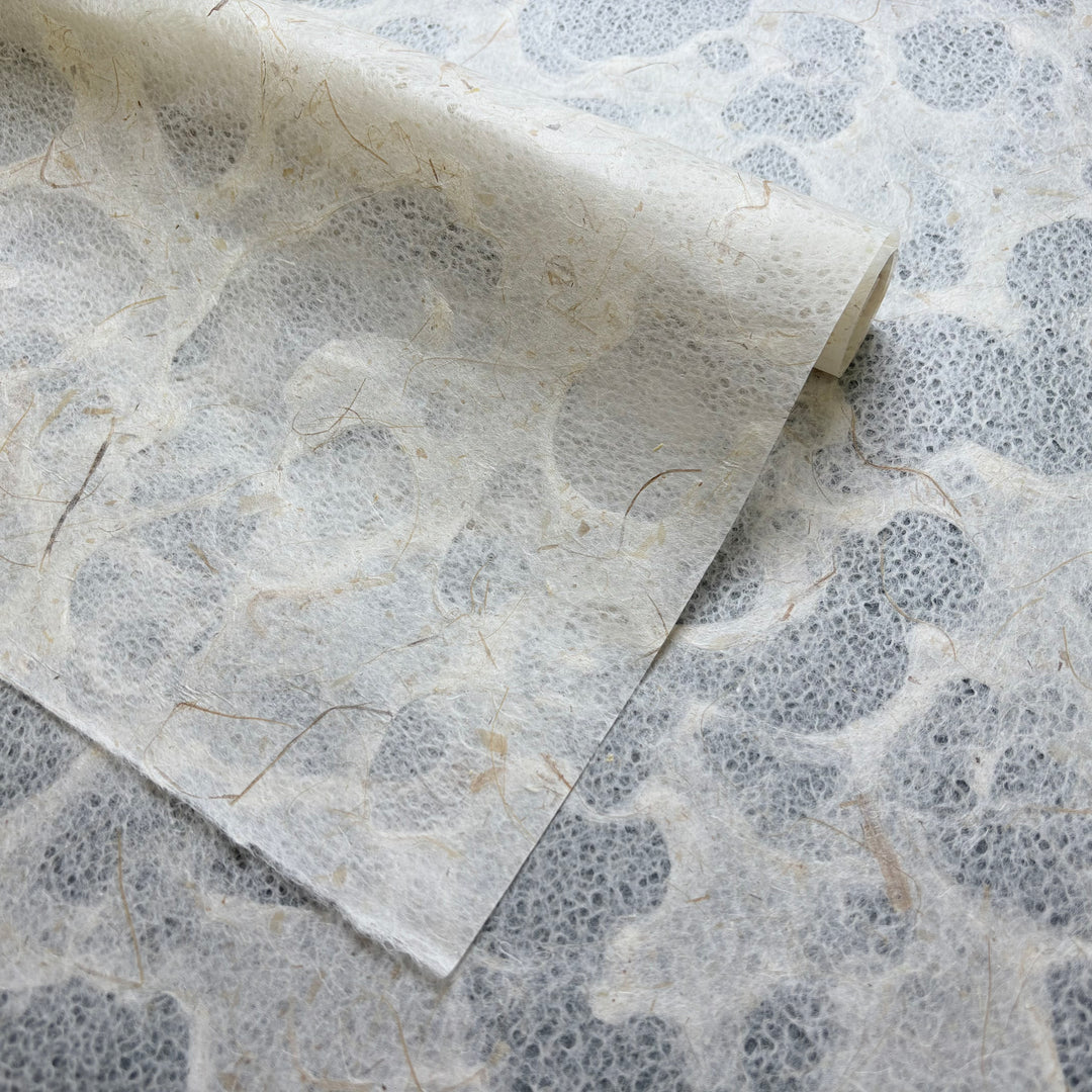 A close-up of Kozo Studio’s Tidal Lace Kozo Paper (Banana Fiber), showing its eco-friendly texture, visible natural fibers, and gently curled corner on a matching surface—ideal for mixed-media art projects.