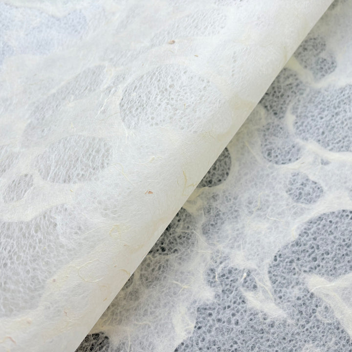 A close-up of Kozo Studio’s Tidal Lace Kozo Paper (Unryu), showcasing circular patterns and plant fibers—an eco-conscious, handmade paper artistically folded to highlight its sustainable materials.