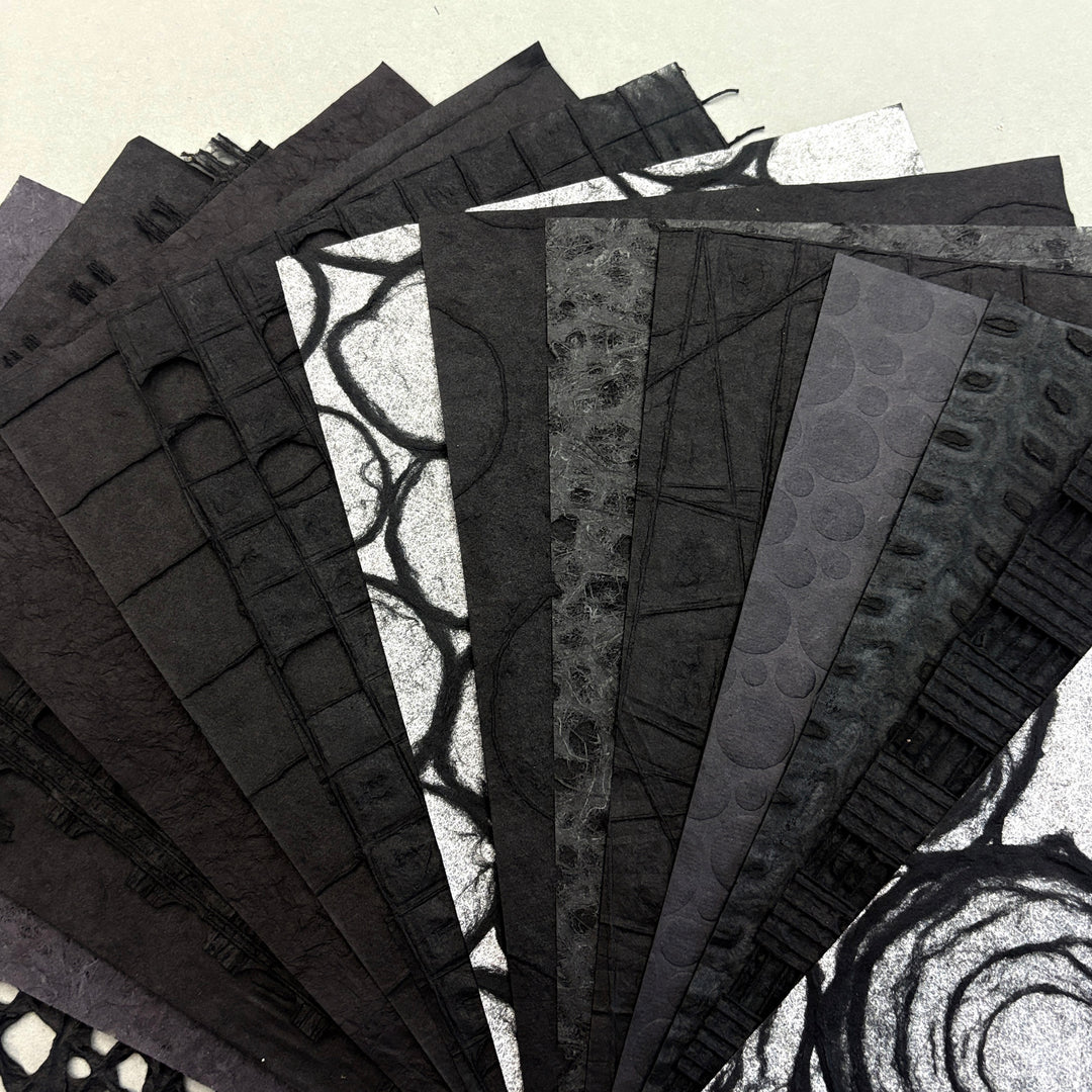A fan arrangement of textured black and gray patterned paper sheets on a light beige background.