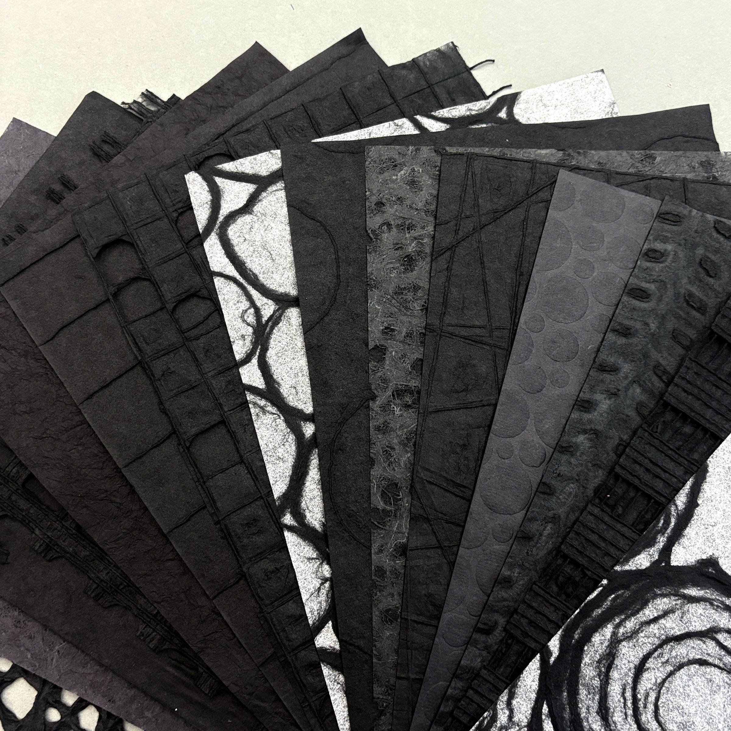 A fan arrangement of textured black and gray patterned paper sheets on a light beige background.