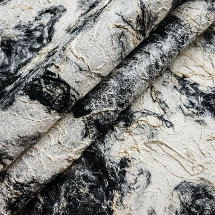 Close-up of handmade mulberry paper from Kozo Studio showcasing a rough textured surface and a black and white earthy color blend.