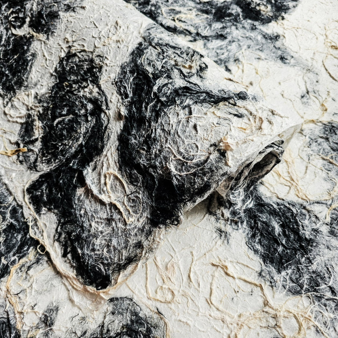 A sheet of Kozo Studio mulberry paper featuring a textured, medium-weight surface with a natural black and white color mix.