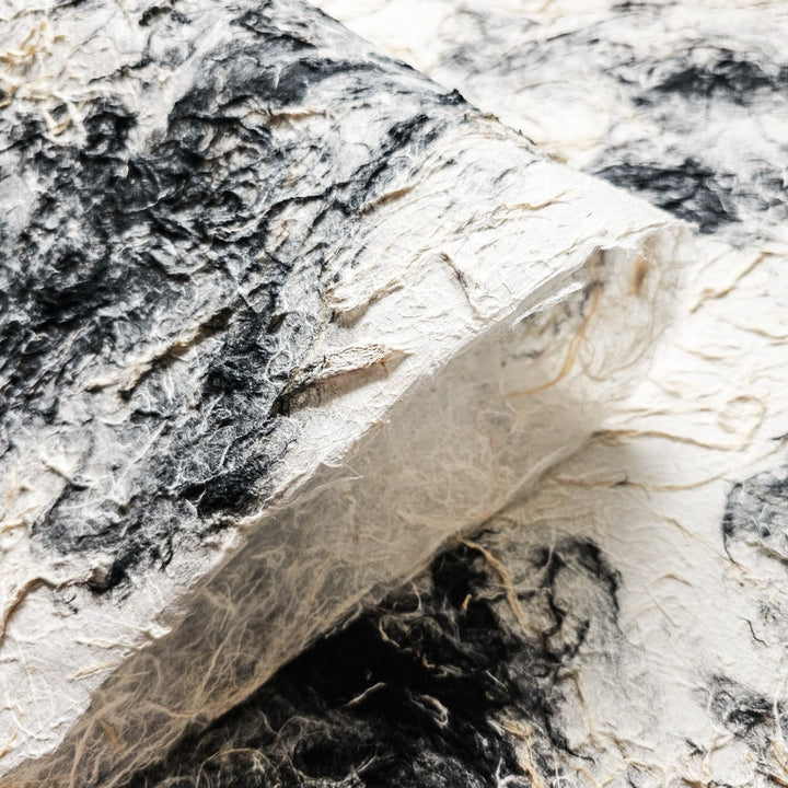 A close-up of Handmade Earthy Harmony Kozo Paper by Kozo Studio shows textured black and white marbled patterns. The fibrous, layered paper has a rough appearance with black swirls contrasting against the white background, creating an artistic, abstract design.